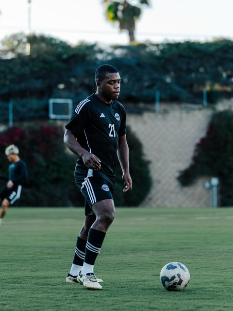 Football player in black jersey number 21 dribbling a ball on grass field during match