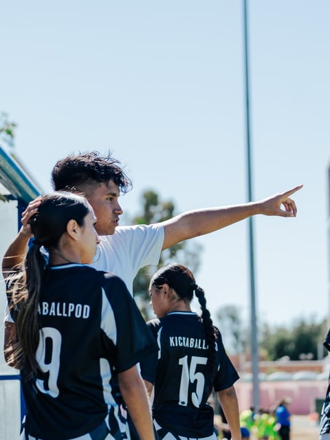 Coach pointing while instructing youth football players in dark uniforms during an outdoor practice or game